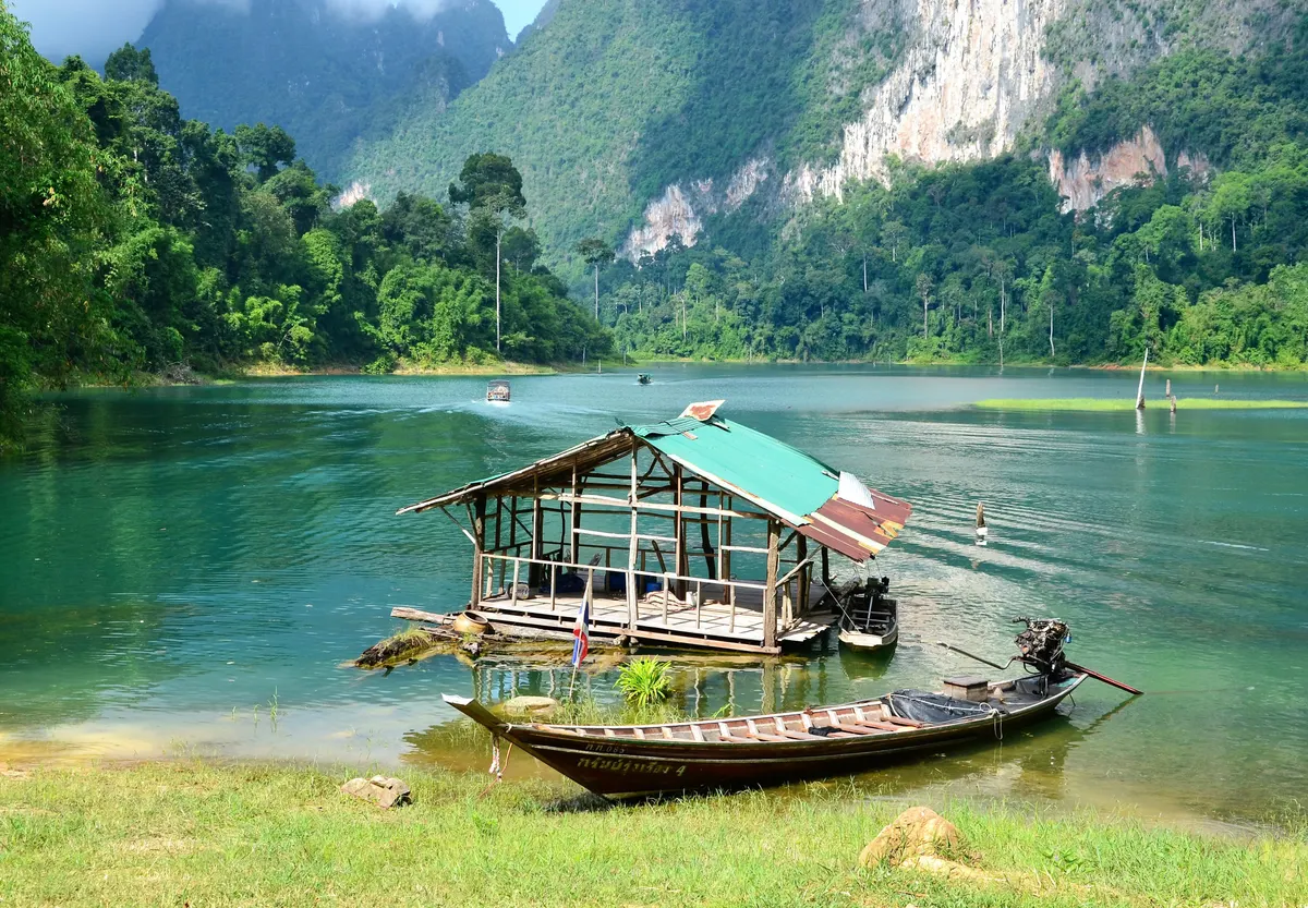 Raft house and longtail boat on the lake in Khao Sok National Park below limestone cliffs