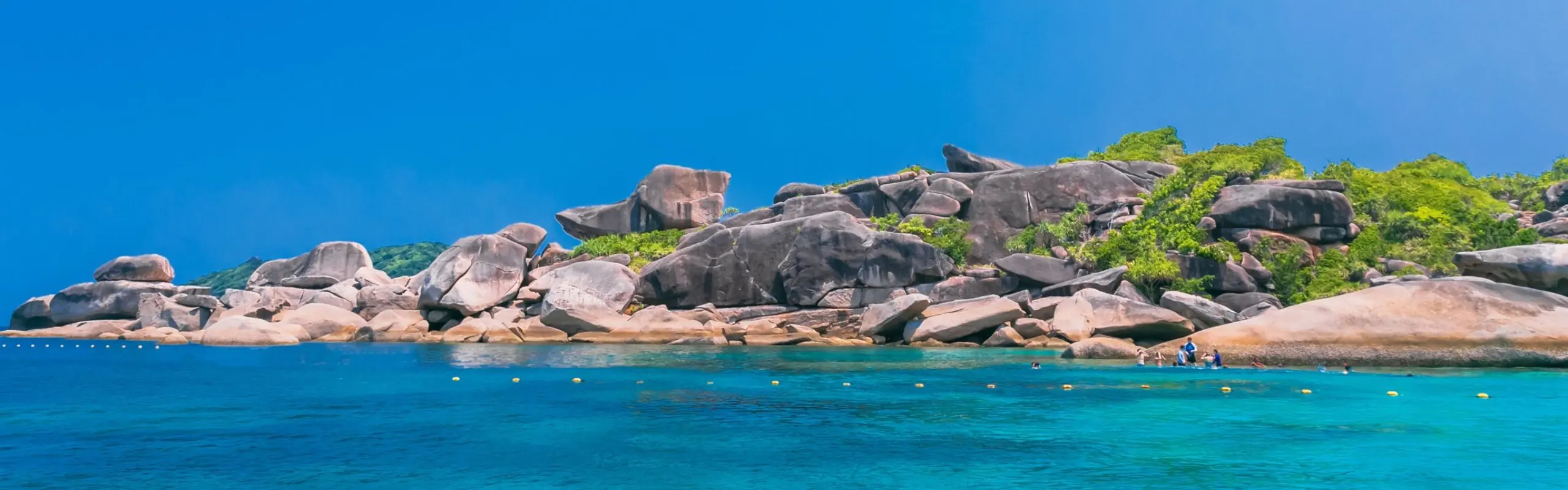 Granite boulders above turquoise water at the Similan Islands, with snorkellers near the shore
